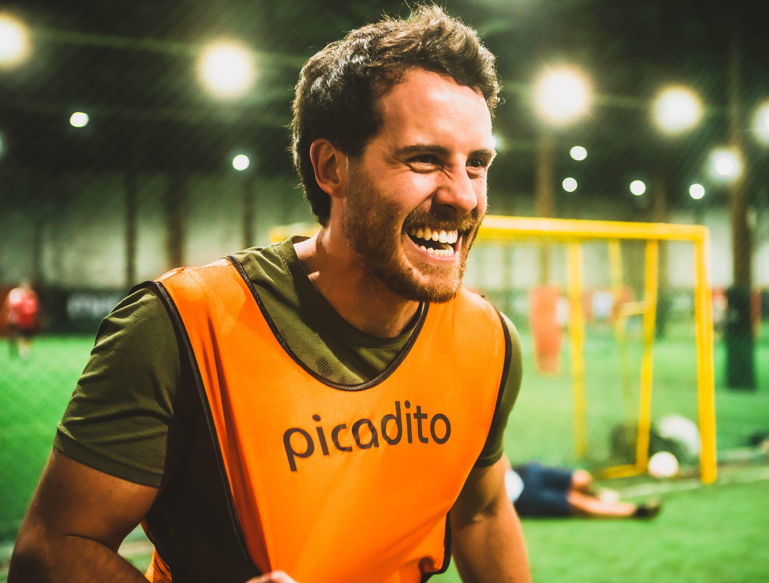 Jugador con pechera naranja de picadito riéndose en la cancha junto a sus compañeros